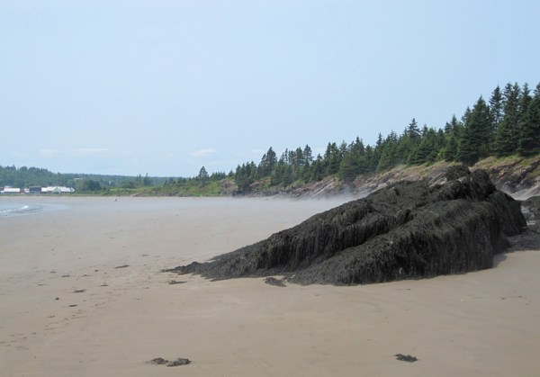 At the far end of the sandy beach, a sloping shelf of bedrock marks the transition . . .